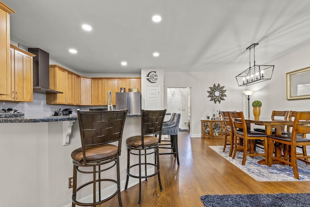 kitchen with stainless steel fridge, tasteful backsplash, dark wood-type flooring, wall chimney range hood, and pendant lighting