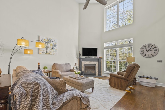 living room with a fireplace, wood-type flooring, ceiling fan, and a high ceiling