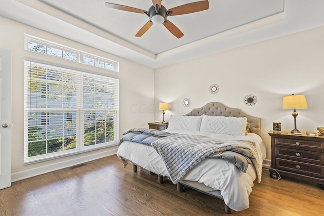 bedroom featuring a raised ceiling, ceiling fan, and dark wood-type flooring