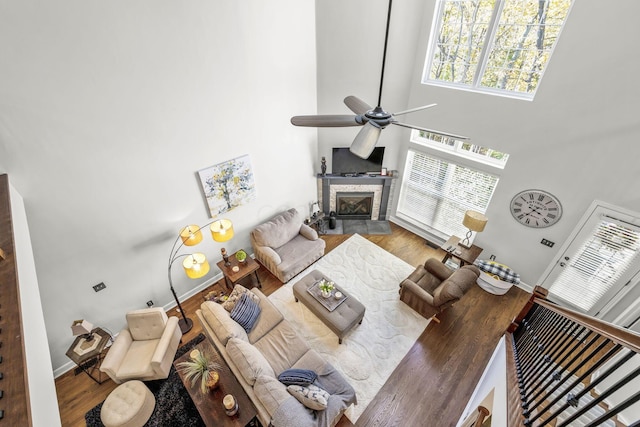 living room featuring a stone fireplace, ceiling fan, a high ceiling, and hardwood / wood-style flooring