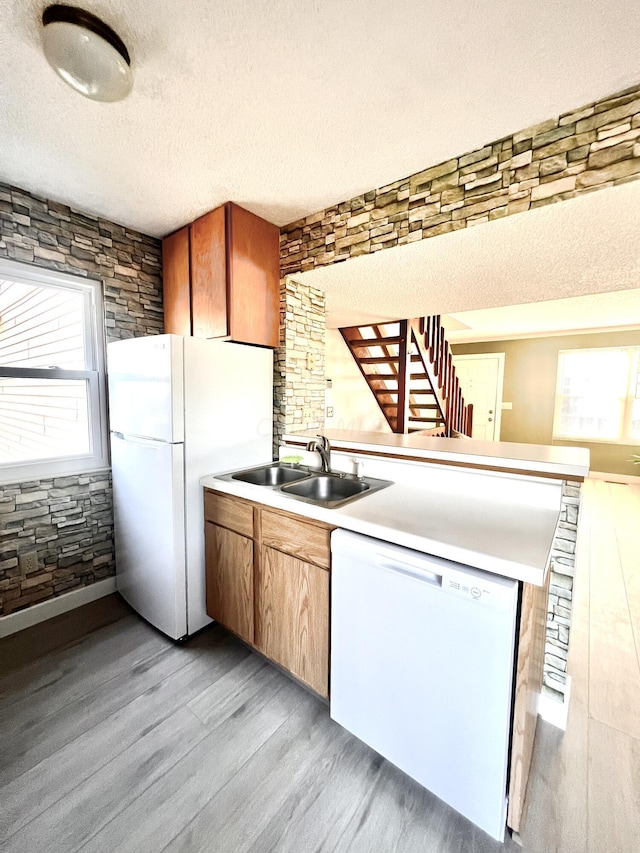 kitchen featuring sink, light hardwood / wood-style flooring, kitchen peninsula, a textured ceiling, and white appliances