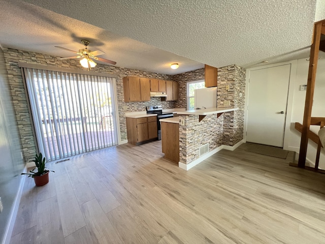 kitchen featuring kitchen peninsula, light hardwood / wood-style floors, a textured ceiling, a kitchen bar, and stainless steel range with electric cooktop