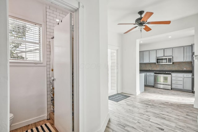 kitchen with appliances with stainless steel finishes, light hardwood / wood-style floors, backsplash, and gray cabinets