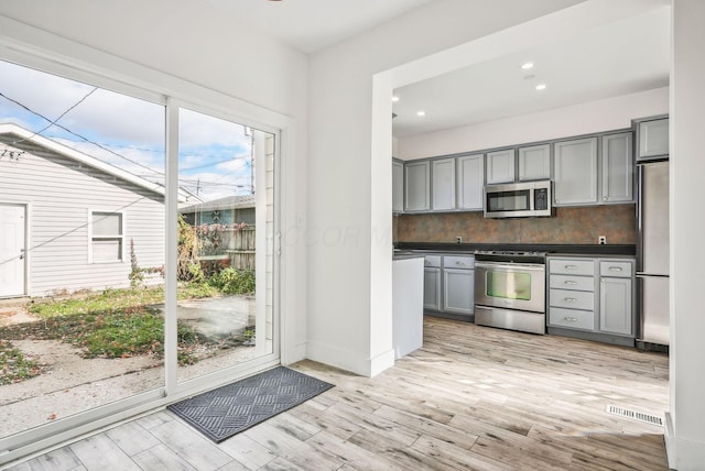 kitchen with appliances with stainless steel finishes, gray cabinetry, light hardwood / wood-style flooring, and backsplash