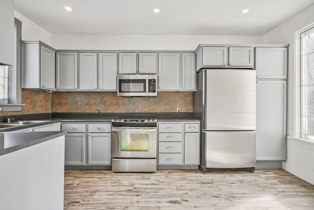 kitchen with sink, appliances with stainless steel finishes, gray cabinetry, and light hardwood / wood-style flooring