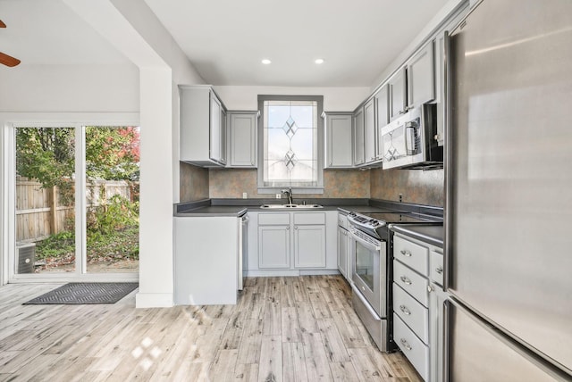 kitchen with backsplash, gray cabinets, sink, light hardwood / wood-style flooring, and stainless steel appliances