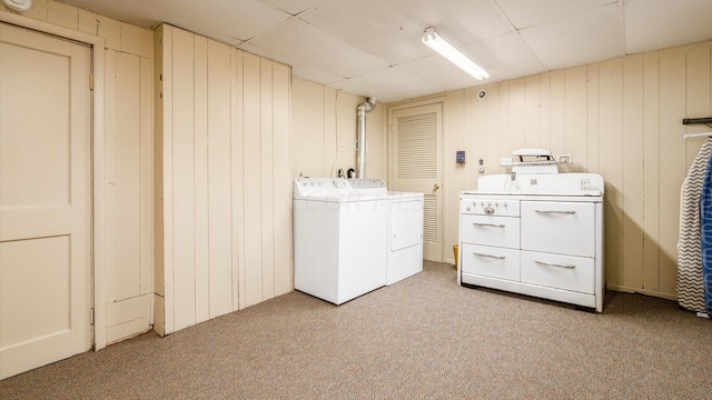 clothes washing area with washer and clothes dryer, light carpet, and wooden walls