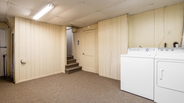 clothes washing area with washing machine and dryer, light carpet, and wooden walls