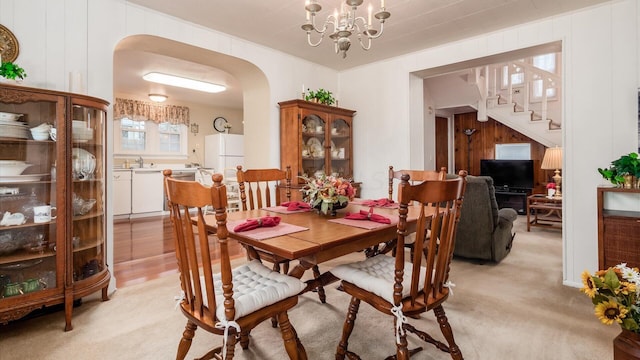 dining area with wood walls, sink, light carpet, and a notable chandelier