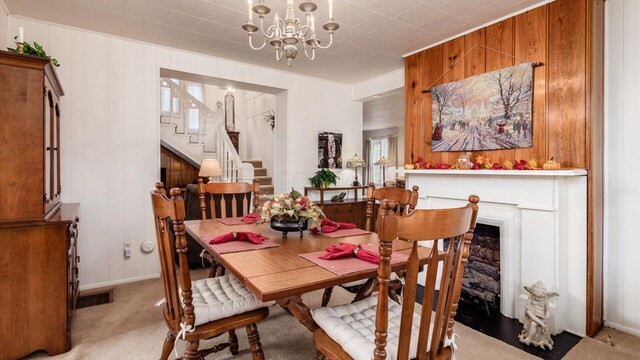 carpeted dining room featuring a healthy amount of sunlight, an inviting chandelier, and wooden walls