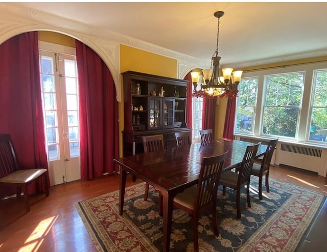 dining room with radiator heating unit, dark wood-type flooring, a healthy amount of sunlight, and a notable chandelier