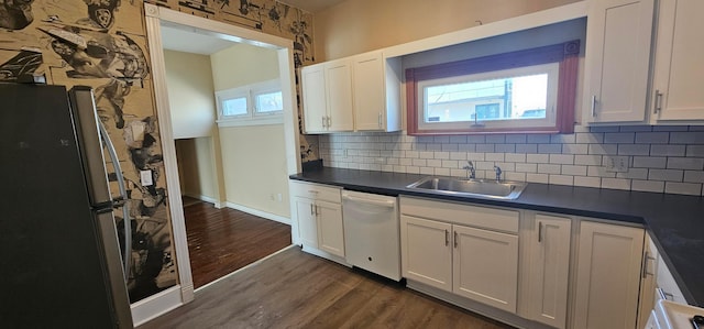 kitchen with a sink, dark wood finished floors, dark countertops, freestanding refrigerator, and white dishwasher