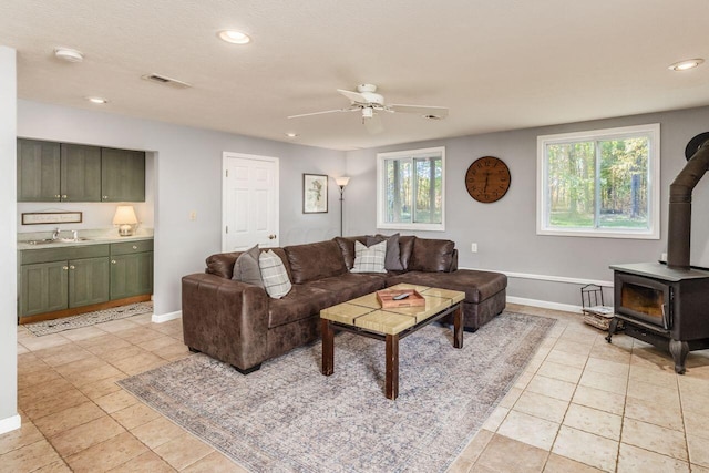 tiled living room featuring a wood stove, a wealth of natural light, sink, and ceiling fan