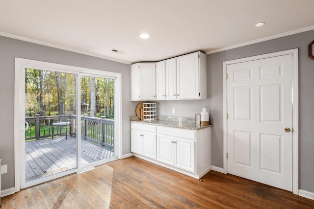 kitchen with white cabinets, light stone counters, wood-type flooring, and ornamental molding