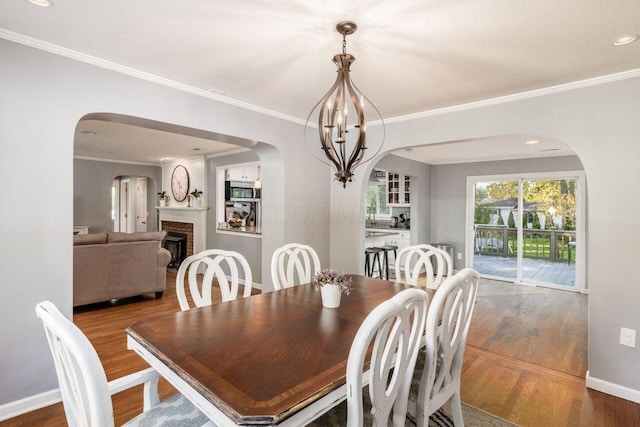 dining room with a fireplace, wood-type flooring, crown molding, and a notable chandelier