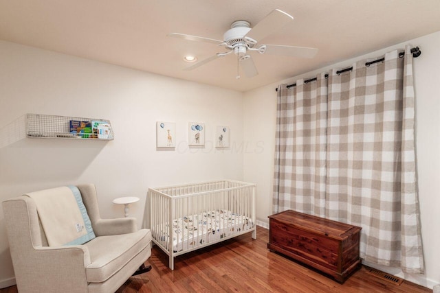 bedroom featuring ceiling fan, hardwood / wood-style floors, and a crib