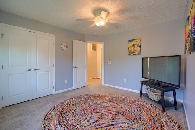 bedroom with a closet, a textured ceiling, light colored carpet, and ceiling fan