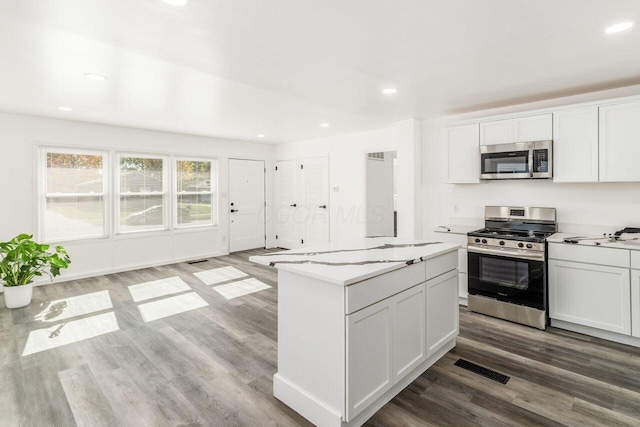 kitchen with light hardwood / wood-style flooring, white cabinets, a kitchen island, and appliances with stainless steel finishes