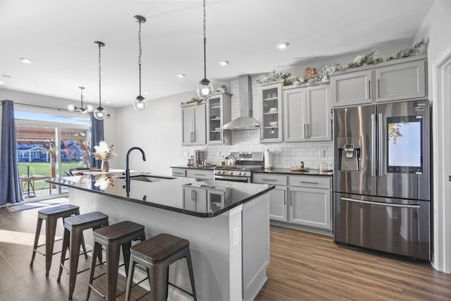 kitchen with sink, wall chimney range hood, a kitchen bar, a center island with sink, and appliances with stainless steel finishes