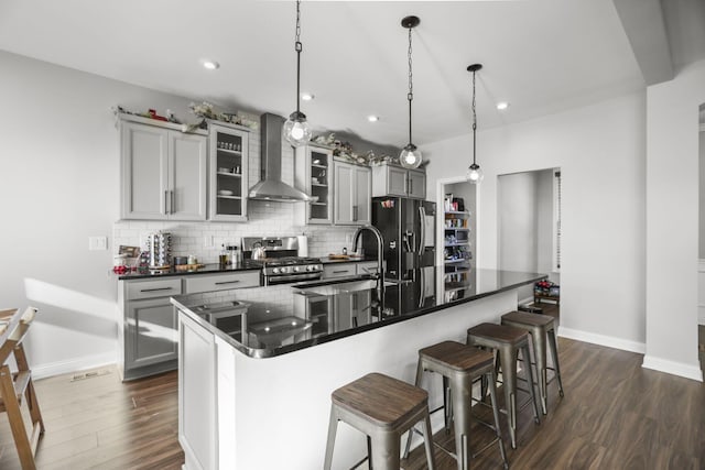 kitchen with sink, stainless steel appliances, wall chimney range hood, dark hardwood / wood-style flooring, and a breakfast bar