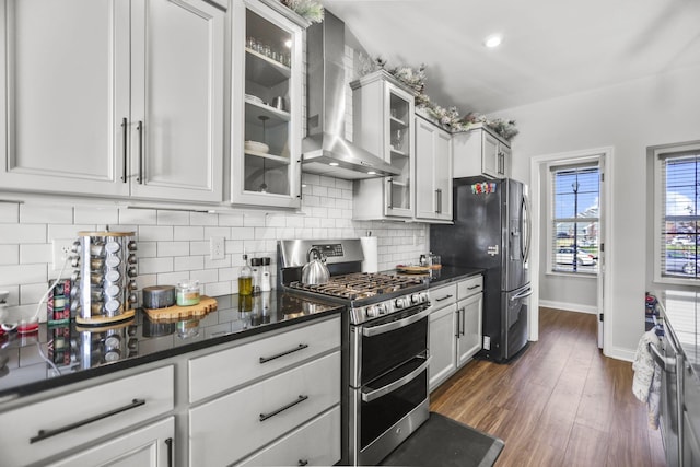 kitchen with wall chimney range hood, dark hardwood / wood-style floors, backsplash, white cabinets, and appliances with stainless steel finishes