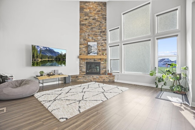 living room with hardwood / wood-style floors, a stone fireplace, and a high ceiling