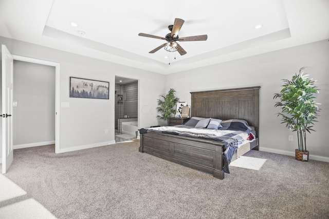 carpeted bedroom with a tray ceiling, ensuite bathroom, and ceiling fan