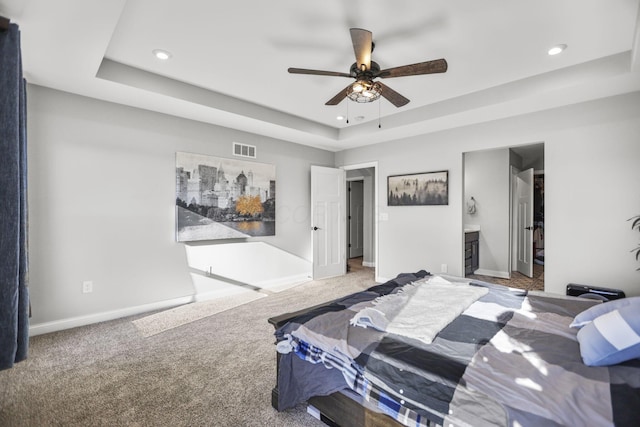 bedroom with carpet flooring, ceiling fan, a tray ceiling, and ensuite bath