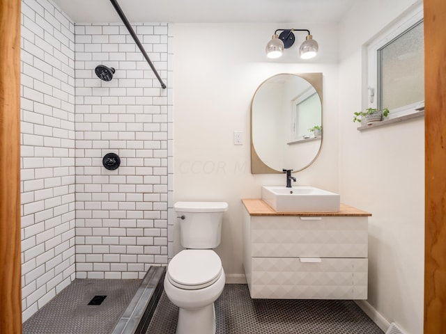 bathroom with tile patterned flooring, vanity, toilet, and a tile shower