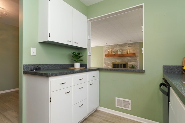 kitchen featuring light hardwood / wood-style flooring, a fireplace, dishwashing machine, white cabinetry, and brick wall