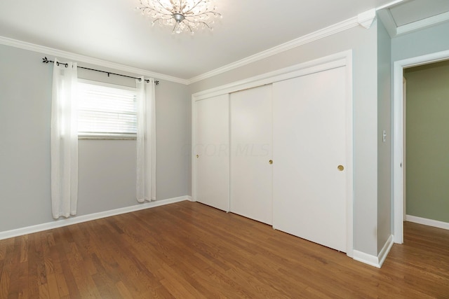 unfurnished bedroom featuring hardwood / wood-style flooring, an inviting chandelier, a closet, and ornamental molding