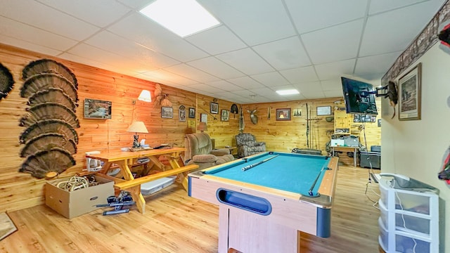 recreation room with light wood-type flooring, pool table, a paneled ceiling, and wood walls