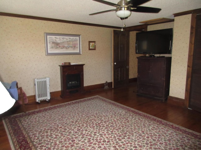 unfurnished living room with dark wood-type flooring, radiator, ceiling fan, ornamental molding, and a textured ceiling