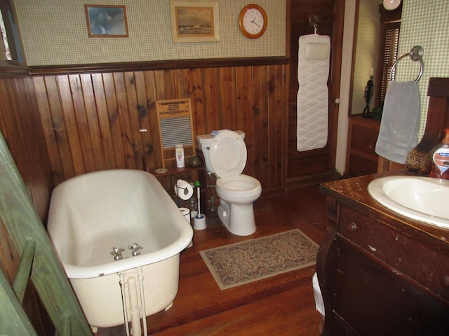 bathroom with a washtub, hardwood / wood-style floors, toilet, wooden walls, and vanity