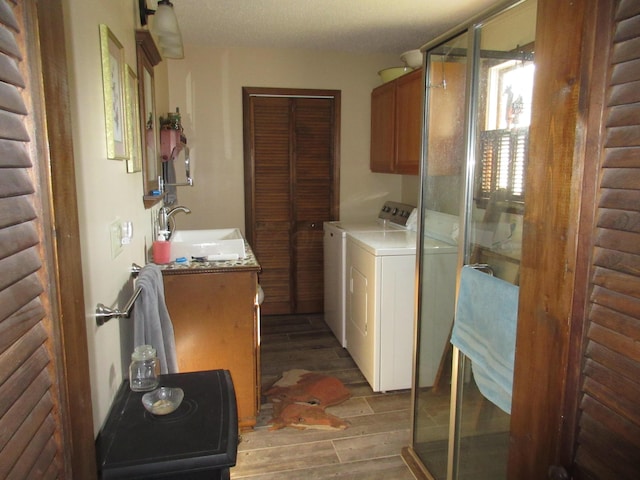 clothes washing area featuring sink, cabinets, light hardwood / wood-style floors, a textured ceiling, and washer and dryer