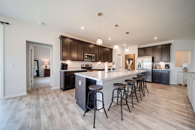 kitchen featuring a center island with sink, light wood-type flooring, decorative light fixtures, a kitchen bar, and stainless steel appliances