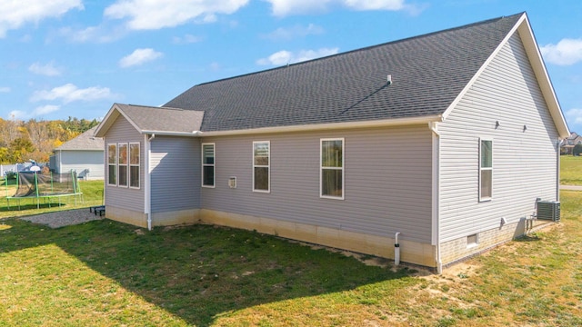 rear view of property with a lawn, central AC, and a trampoline