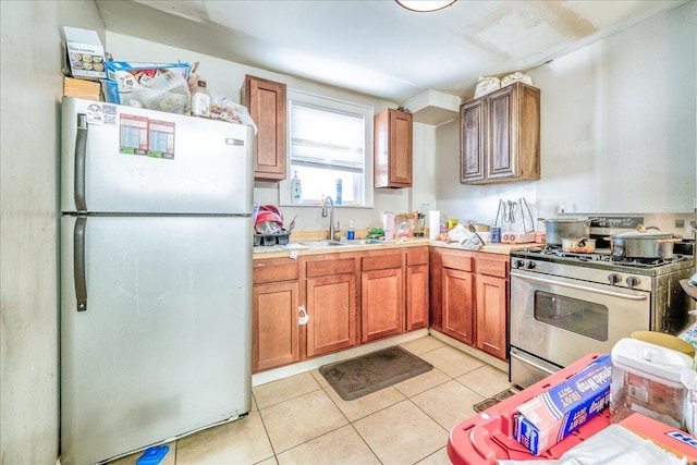 kitchen with stainless steel gas range oven, sink, white fridge, and light tile patterned floors