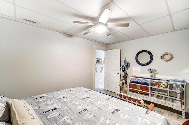 bedroom featuring ceiling fan, a drop ceiling, and wood-type flooring