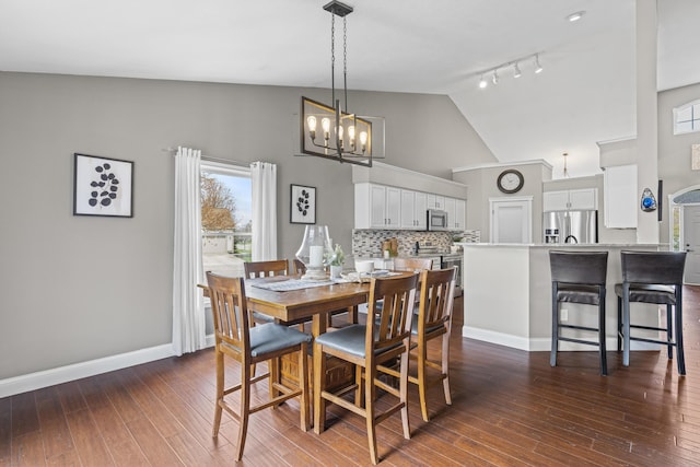 dining area featuring baseboards, an inviting chandelier, rail lighting, dark wood finished floors, and high vaulted ceiling