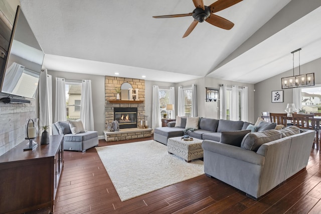 living room featuring a stone fireplace, recessed lighting, dark wood-type flooring, lofted ceiling, and ceiling fan with notable chandelier