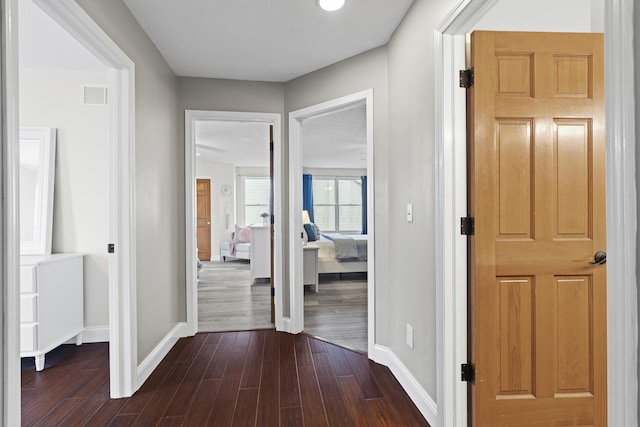hall with visible vents, baseboards, and dark wood finished floors