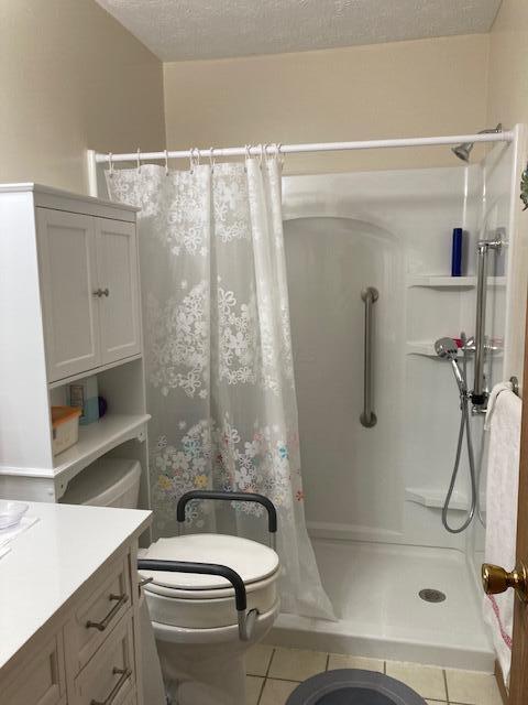 bathroom with a shower with curtain, a textured ceiling, vanity, tile patterned flooring, and toilet