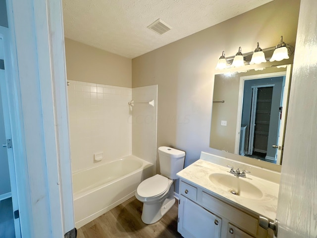 full bathroom featuring wood-type flooring, a textured ceiling, toilet, shower / washtub combination, and vanity