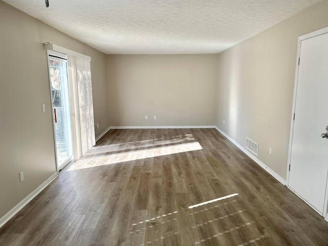 empty room with a textured ceiling, plenty of natural light, and dark wood-type flooring