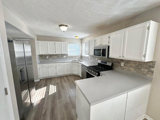 kitchen with white cabinetry, sink, stainless steel appliances, kitchen peninsula, and light hardwood / wood-style floors