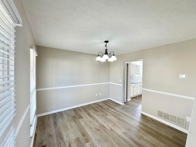 spare room with hardwood / wood-style floors, a textured ceiling, and a notable chandelier