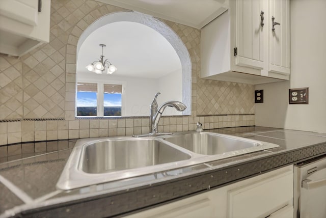 kitchen with dishwasher, backsplash, white cabinets, sink, and a chandelier