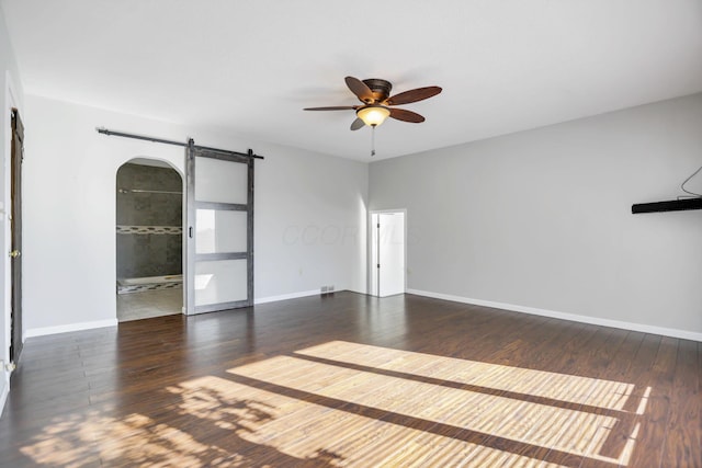 unfurnished room featuring a barn door, dark hardwood / wood-style floors, and ceiling fan