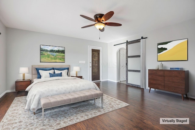 bedroom featuring a barn door, dark hardwood / wood-style floors, and ceiling fan